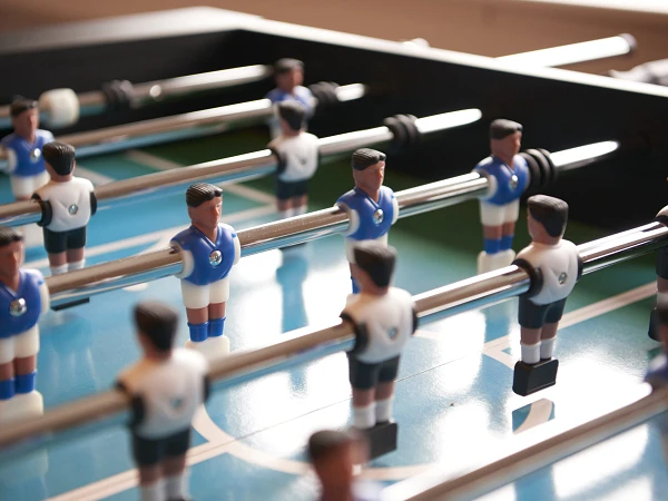 Detailaufnahme eines Kickertischs mit blauen und weißen Spielfiguren