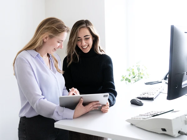 Zwei Frauen im Gespräch an einem Schreibtisch mit Tablet