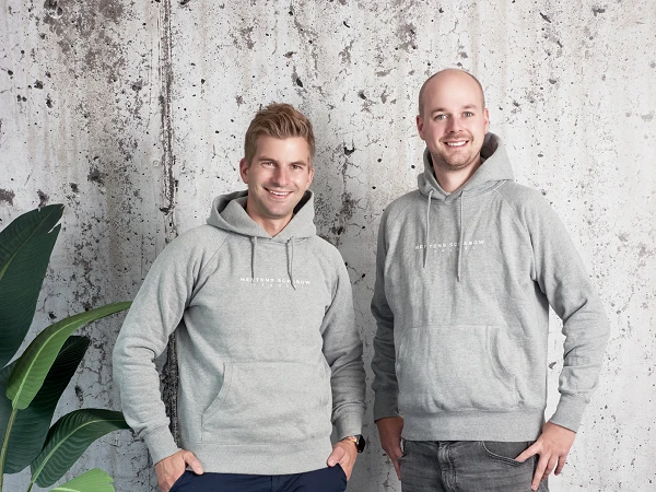 Foto von zwei Männern in grauen Hoodies vor einer Steinwand