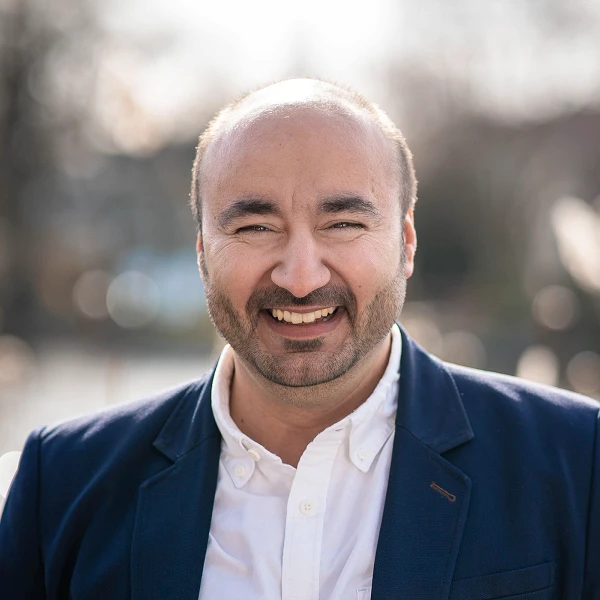 Lächelnder Mann im dunklen Sakko vor Wasser mit Bokeh im Hintergrund