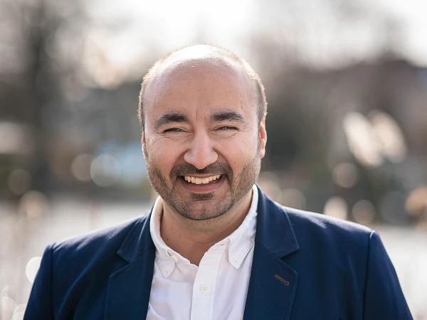 Lächelnder Mann im dunklen Sakko vor Wasser mit Bokeh im Hintergrund