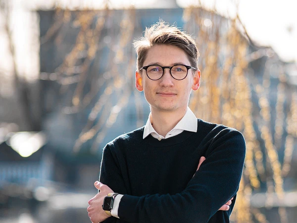 Mann mit Brille im dunklen Pullover vor Wasser und Lichtreflexen