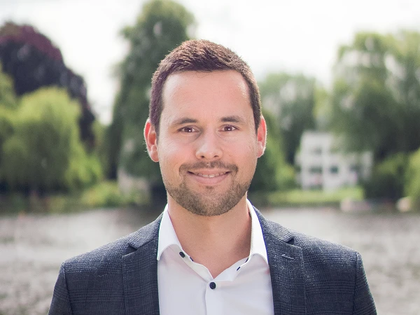 Mann im dunklen Sakko vor Flusslandschaft
