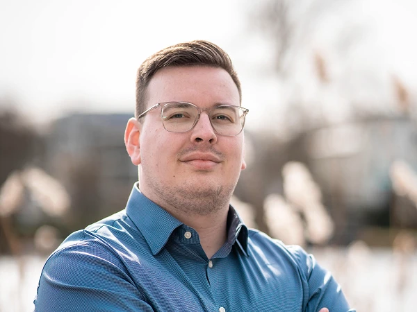 Mann mit Brille und blauem Hemd, verschränkt die Arme vor See