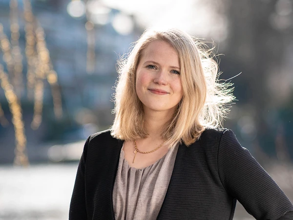 Frau mit dunkelblondem Haar im Blazer, lächelt vor Flusslandschaft