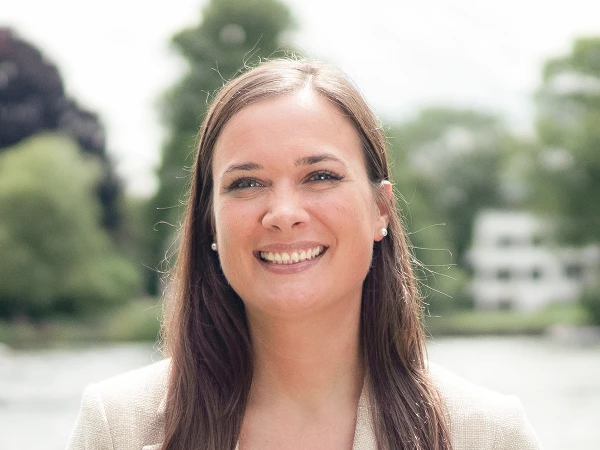 Frau mit brauen Haaren im beigen Blazer am Wasser