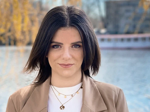 Frau mit kurzem braunen Haar im braunen Blazer am Seeufer